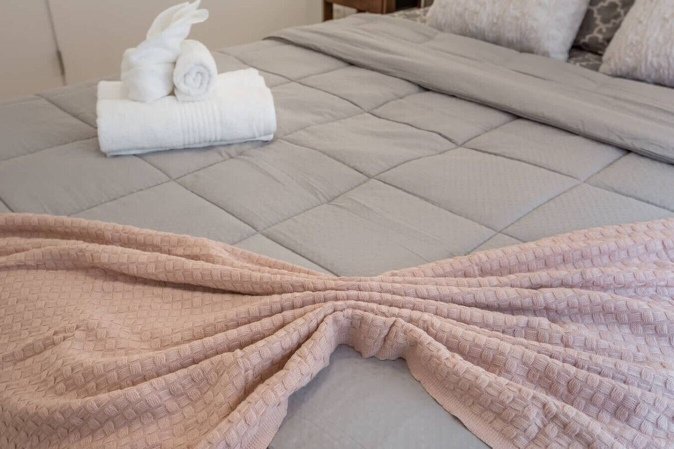 Una cama con cabecera acolchada, una toalla blanca doblada y una manta rosa.