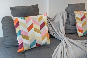 Ein graues Sofa mit zwei farbenfrohen Kissen in Zickzackmuster und einer grauen Decke.