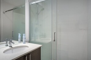 Un bagno moderno con box doccia in vetro, un lavandino bianco con due rubinetti e due flaconi di sapone per le mani.