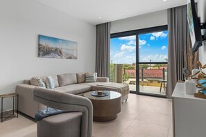 A modern living room with a sectional sofa, a round coffee table, and a large window offering a view of the outdoors. - Close to Eagle Beach·Balcony·Pool & Jacuzzi·BBQ & (Eagle)