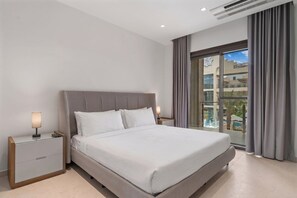 Camera d'albergo moderna con un letto grande, un comodino, una lampada e vista su una piscina attraverso una porta vetrata.