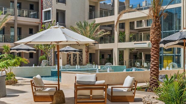 Zona de piscina amb gandules, ombrel·les i una font.