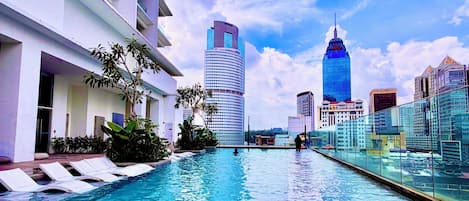 A swimming pool with lounge chairs, a modern building, and a city skyline in the background.