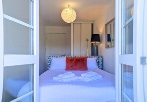 Ein Hotelzimmer mit Bett, Nachttisch, Lampe, Spiegel und Tür.