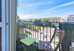 Ein Balkon mit Blick auf eine Straße, ein grüner Stuhl und eine hölzerne Bank.