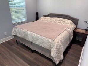 A bedroom with a bed, a nightstand, a lamp, and a window with blinds.
