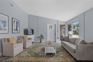 Ein Wohnzimmer mit zwei Sofas, einem Couchtisch, einem Fernseher und einer Tür, die nach draußen führt.