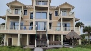 A multi-story beachfront hotel with a central staircase, balconies, and a thatched structure. - Plantation at St George Island Fl. Beautiful beach view from all bedrooms (East Point)