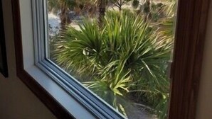 A view through a window of a beachfront property with a large building and palm trees. - Plantation at St George Island Fl. Beautiful beach view from all bedrooms (East Point)