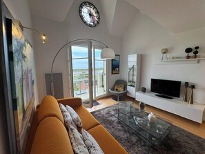 A modern living room with a sofa, a glass coffee table, a TV, and a fireplace. - Apartment with sea view, terrace and swimming pool (Dives-sur-Mer)