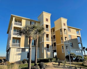 Un immeuble résidentiel à plusieurs étages, doté de balcons, d’un palmier et surplombant un ciel bleu azur.