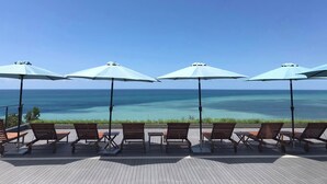 Eine Terrasse mit Liegestühlen und Sonnenschirmen mit Blick auf das klare, blaue Meer.