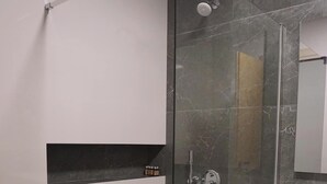 Ein modernes Badezimmer mit einer gläsernen Duschkabine, einem integrierten Waschbecken und einem Mülleimer.