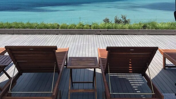 Eine Holzterrasse mit Liegestühlen und Sonnenschirmen mit Blick auf ein klares, blaues Meer.