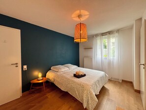 Un dormitorio con cama, mesita de noche, lámpara y ventana con cortinas.