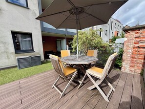 Eine Terrasse im Freien mit einem runden Holztisch, gelb gepolsterten Stühlen und einem großen Sonnenschirm.