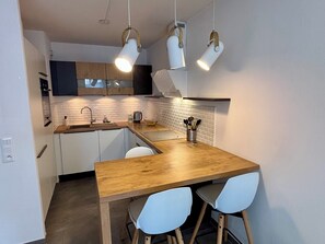 Una cocina moderna con una isla de madera, sillas blancas, un lavamanos y lámparas colgantes.
