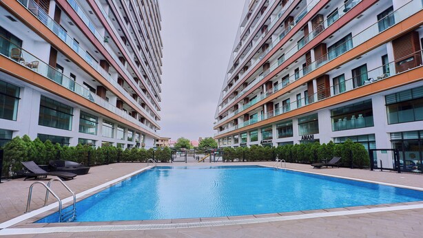 Ein modernes Hotel mit einem zentralen Schwimmbad, mehreren Balkonen und blauem Himmel.