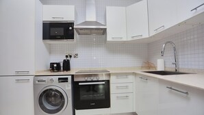 Eine moderne Küche mit weißen Schränken, einer Bosch-Mikrowelle, einem Backofen und einer Waschmaschine.