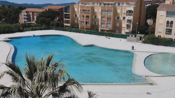 A swimming pool surrounded by buildings with balconies, palm trees, and a clear sky. - Bright apartment with balcony and swimming pool (Fréjus)