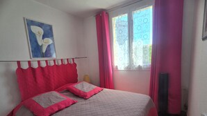 A bedroom with a bed, a painting, a window with curtains, and a radiator. - Bright apartment with balcony and swimming pool (Fréjus)