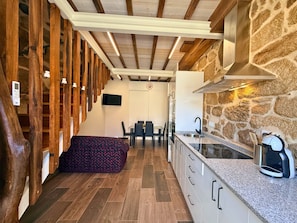 A compact kitchen with stone walls, wooden beams, and a dining area with a table and chairs. - YourHouse A Casa Do Cordeiro (Allariz)