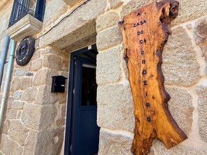 A stone building with a wooden sign reading 'CASA DO CARDERIO' and a black door. - YourHouse A Casa Do Cordeiro (Allariz)