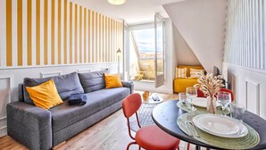 A modern living room with a grey sofa, yellow cushions, a dining table set with plates and glasses, and a view through an open door. - Studio with balcony in Villers-sur-Mer (Villers-sur-Mer)
