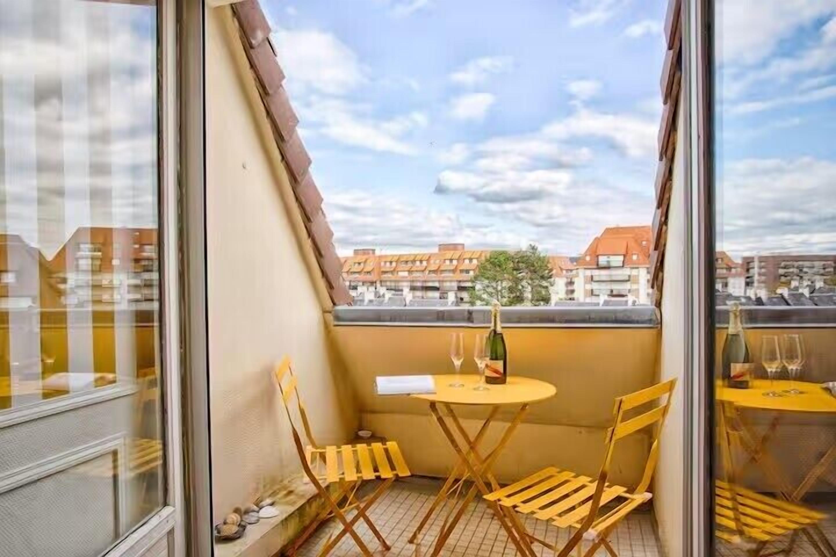 A balcony with a table and chairs, a bottle, and a glass.