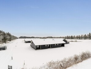 Eine verschneite Landschaft mit mehreren Gebäuden, blauem Himmel und einem Wald im Hintergrund.