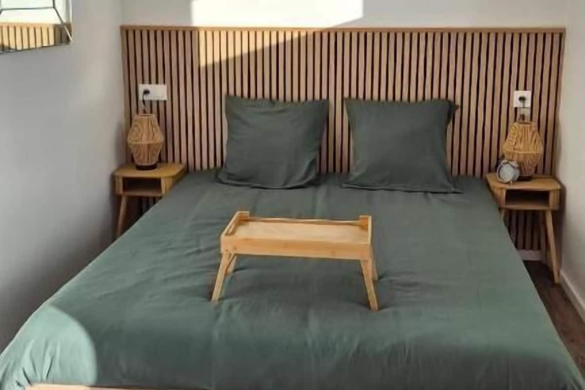 A bedroom with a bed, wooden headboard, bedside tables, a window with a view, and a bedside lamp.