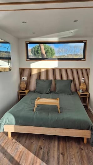 Une chambre à coucher comprenant un lit, une tête de lit en bois, des tables de chevet, une fenêtre avec vue et une lampe de chevet.