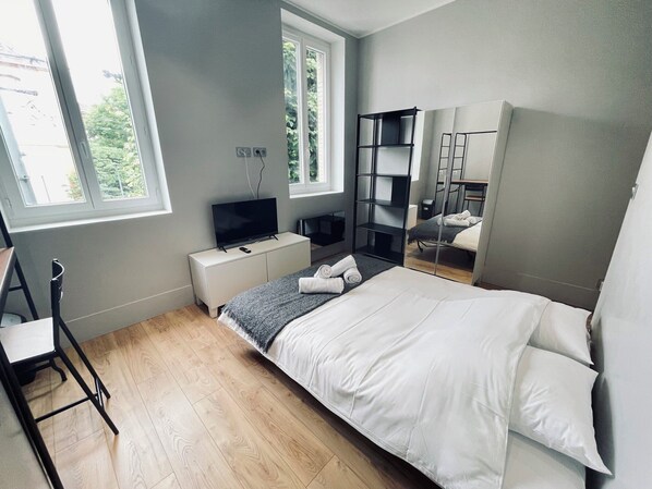 Ein modernes Schlafzimmer mit Bett, Fernseher, Schreibtisch und Spiegel.