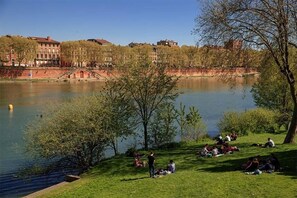 Ein Park mit einem See, Menschen entspannen auf der Wiese, und Gebäude im Hintergrund.