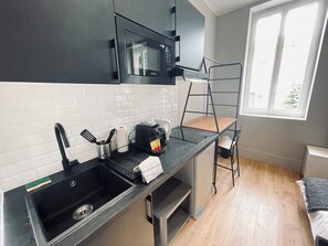 Eine kleine Küche mit schwarzem Arbeitsplatz, einer Mikrowelle, einem Spülbecken und einem Fenster mit Ausblick.