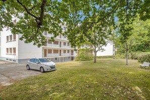 Um edifício branco com um carro estacionado em frente, rodeado por árvores e relva.
