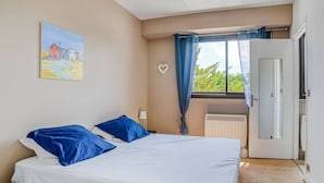 A bedroom with a bed, a radiator, a door, and a window with curtains. - Apartment with balcony and parking near the beach (Arcachon)