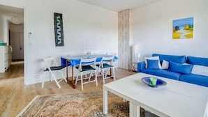 A living room with a blue sofa, a dining table with chairs, and a coffee table. - Apartment with balcony and parking near the beach (Arcachon)