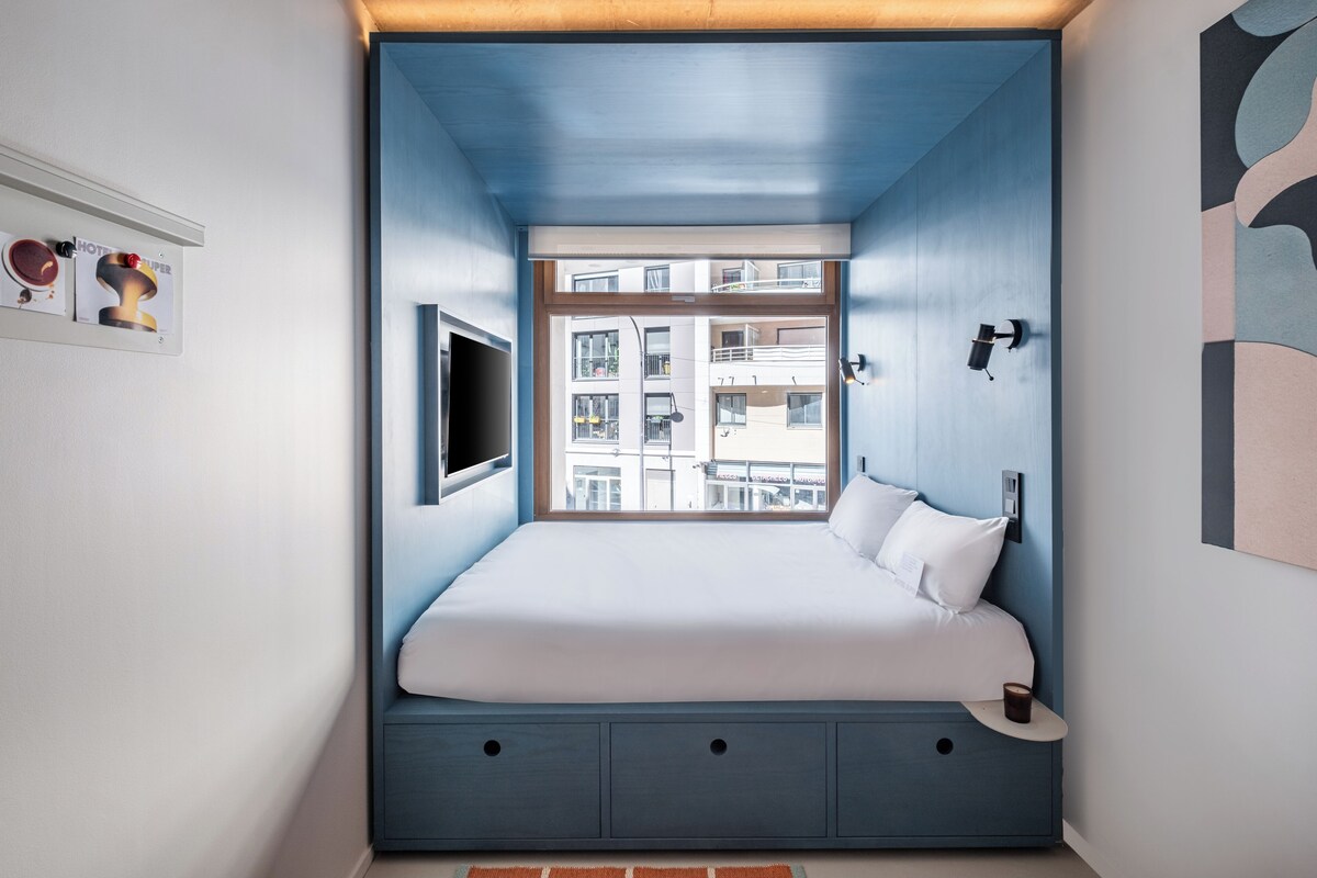 A bedroom with a bed, a window, a wall-mounted TV, and a small table.