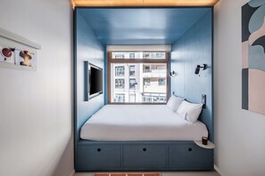 A bedroom with a bed, a window, a wall-mounted TV, and a small table. - Hôtel Super (Paris)