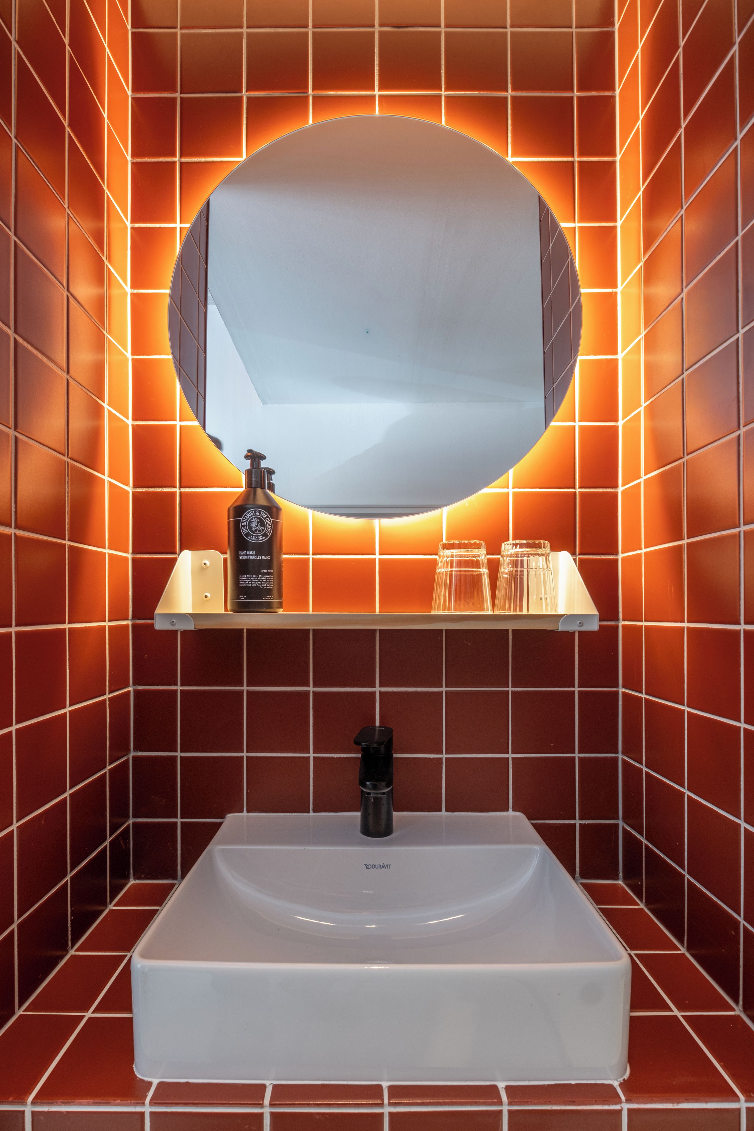 Une salle de bain avec un lavabo blanc, un miroir et une étagère contenant des articles de toilette.