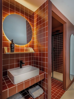 Un baño con un lavamanos grande y rectangular, un espejo redondo y una zona de ducha.