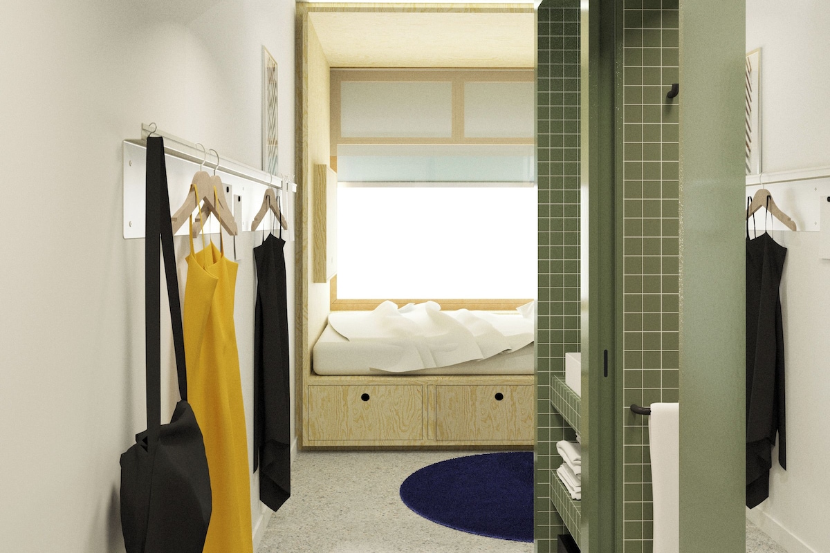 A modern hotel room with a bed, a bathroom, and a hallway.