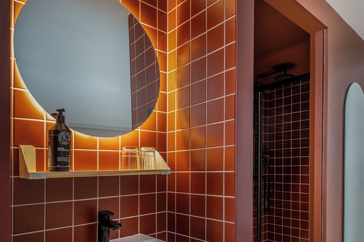 A bathroom with a large rectangular sink, a round mirror, and a shower area.