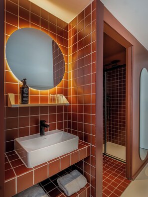 A bathroom with a large rectangular sink, a round mirror, and a shower area. - Hôtel Super (Paris)