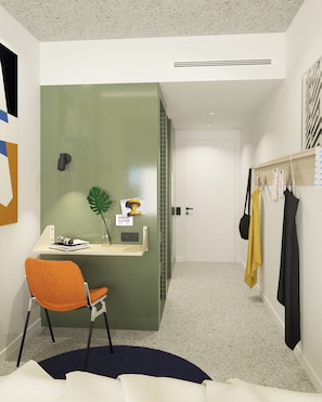 Habitación de hotel con escritorio, una silla, una planta y un perchero con ropa colgada.