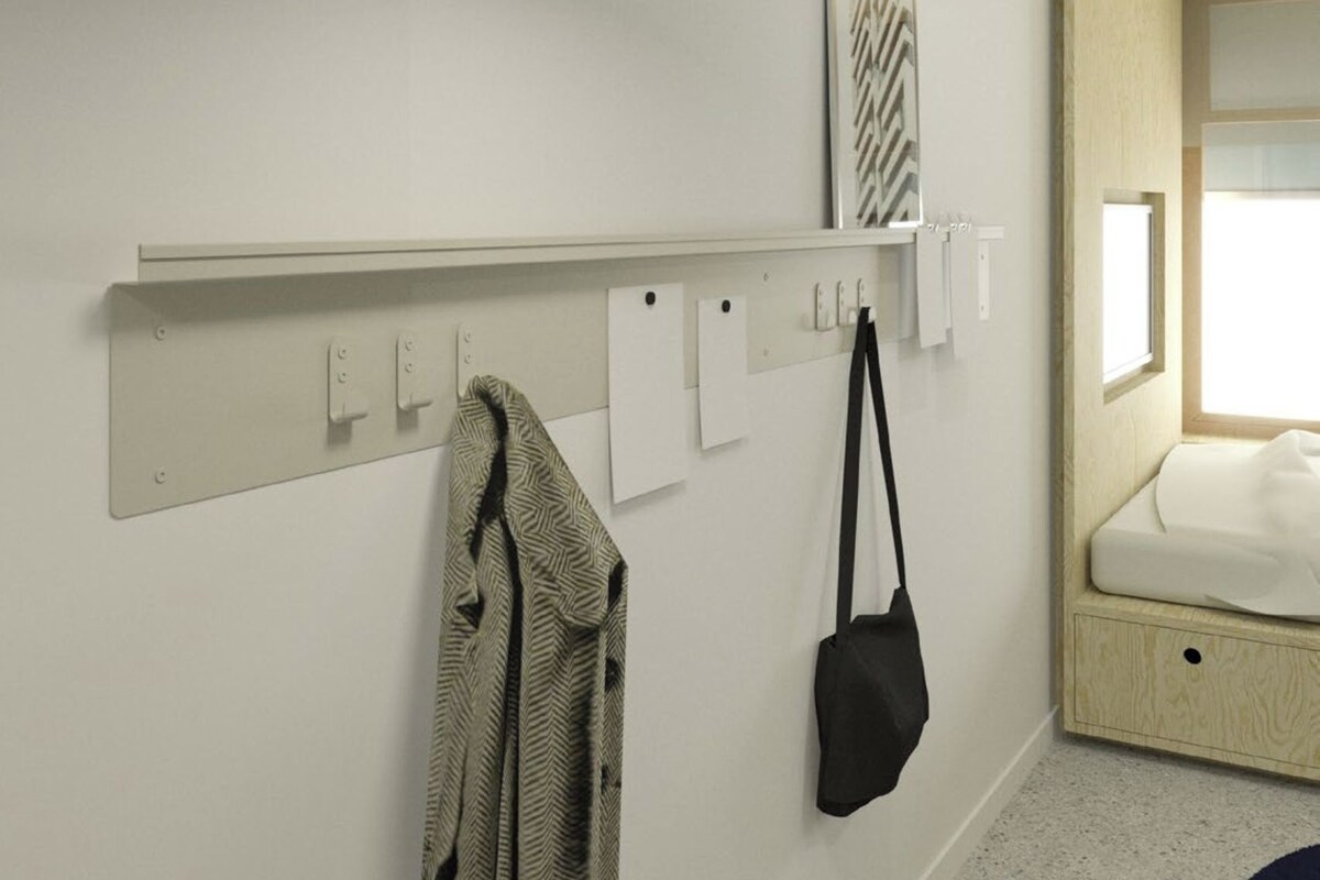 A hotel room with a bed, a wall-mounted shelf, and a coat rack.