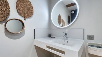 Une salle de bain avec un meuble-lavabo blanc, un miroir rond et deux feuilles décoratives en forme de motifs tissés accrochées au mur.