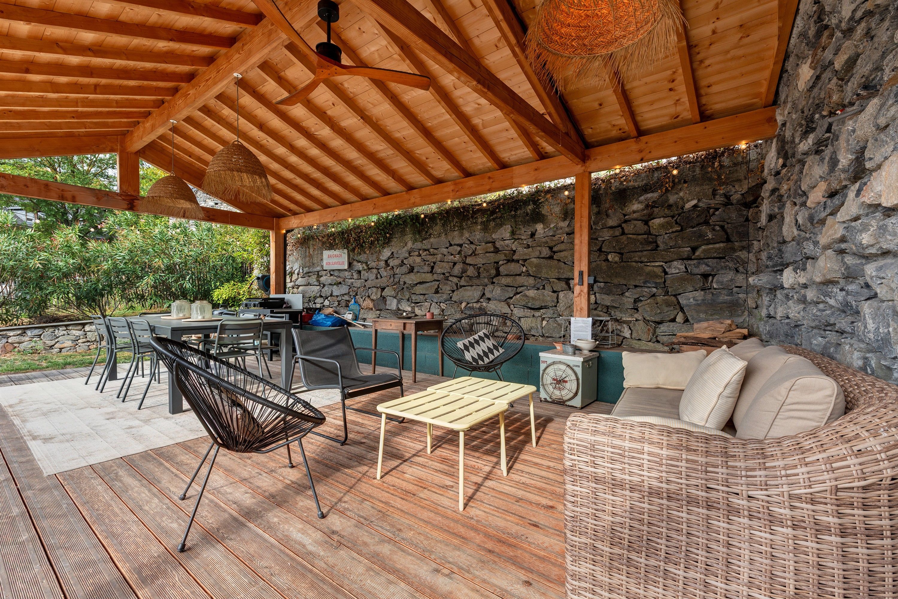 Une terrasse extérieure avec un mur en pierre, un plafond en bois et du mobilier comprenant un canapé, des chaises et une table.