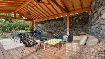 Une terrasse extérieure avec un mur en pierre, un plafond en bois et du mobilier comprenant un canapé, des chaises et une table.